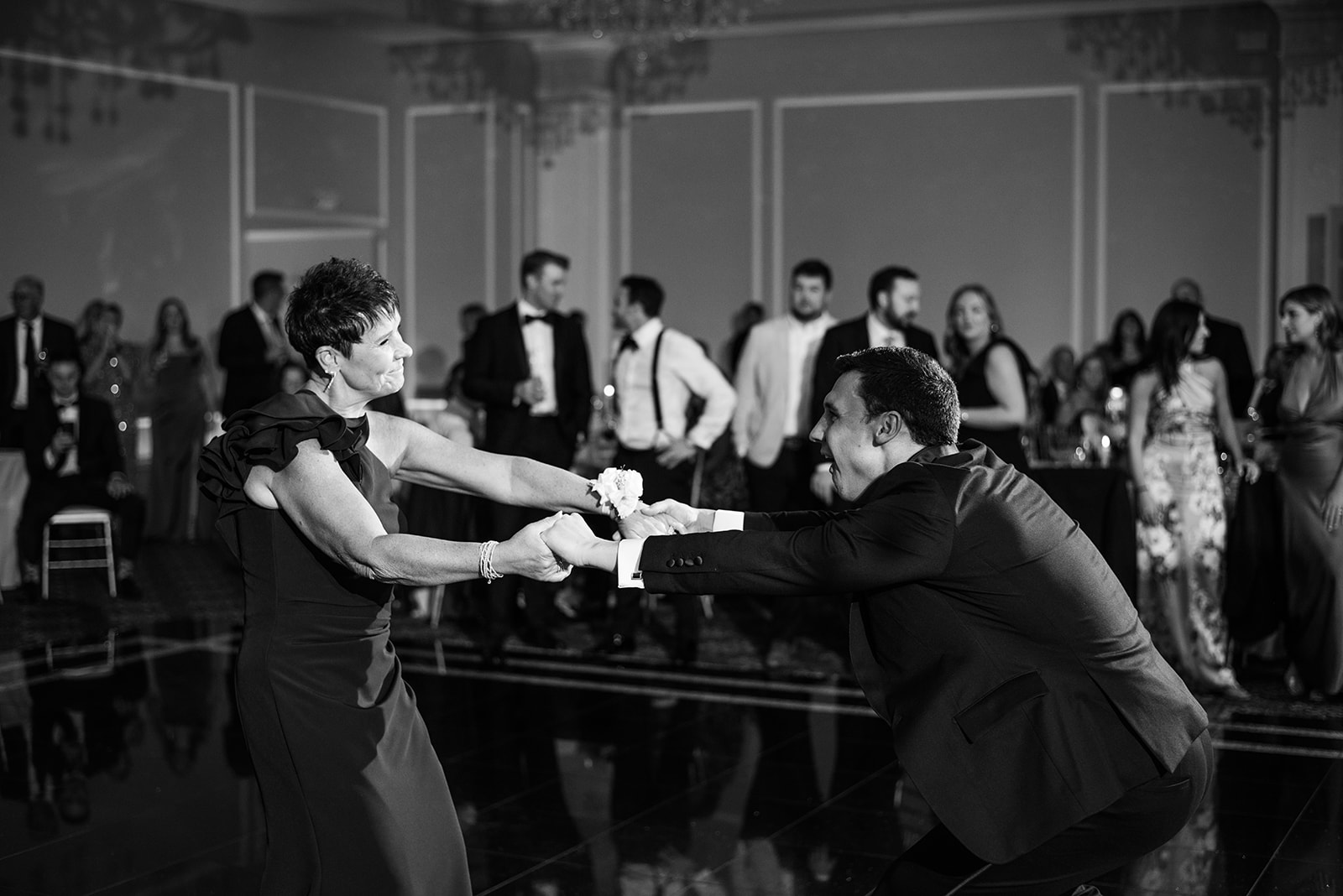Black and white film photo of the groom and his mother dancing dynamically on the reception floor.